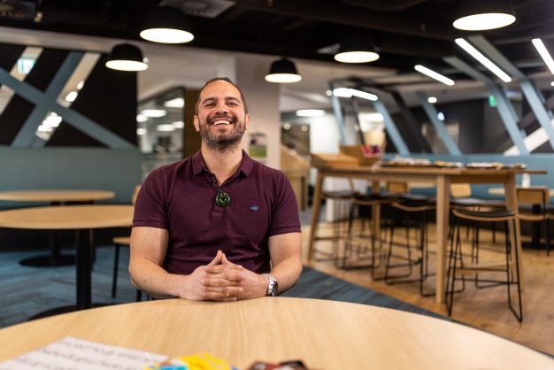 Staff member sits smiling in dining area at National Office, with wooden tables and chairs in the background